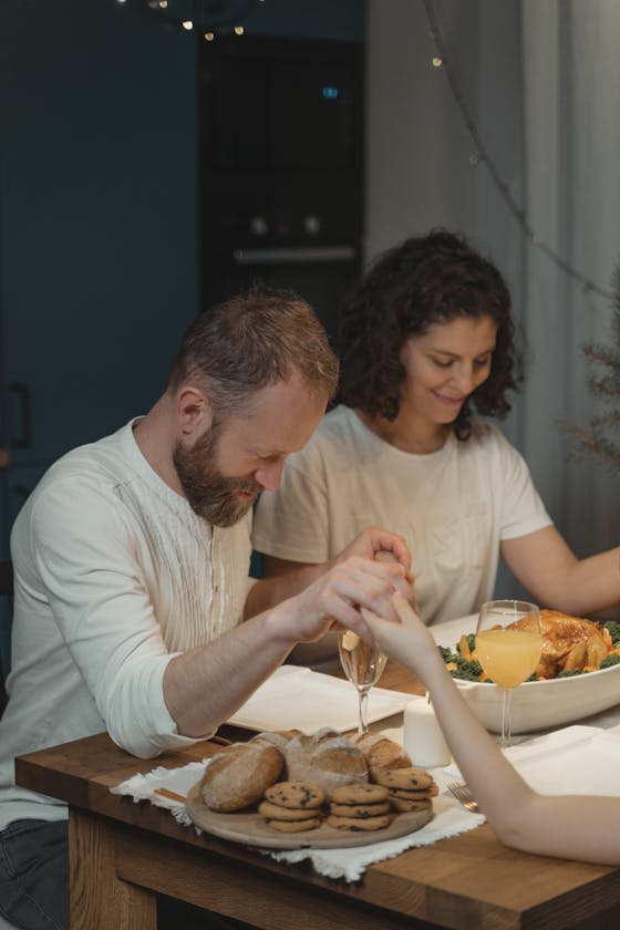 A family gathers around the table, holding hands in prayer before Thanksgiving dinner.