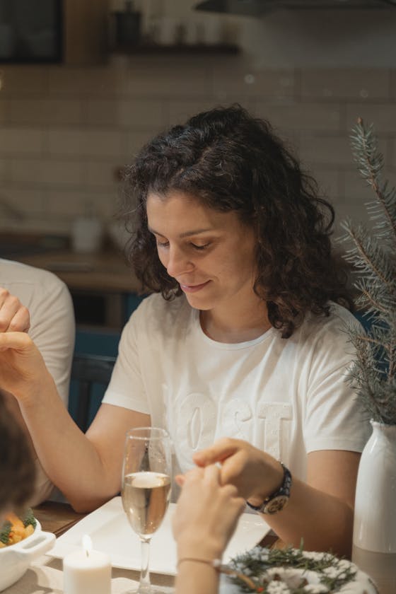 Family gathering around holiday dinner table, holding hands in prayer, creating a warm and festive atmosphere.